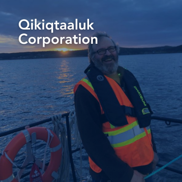 A picture of Dr. Scott Grant on a small boat in the ocean, with the words "Qikiqtaaluk Corporation" written on top